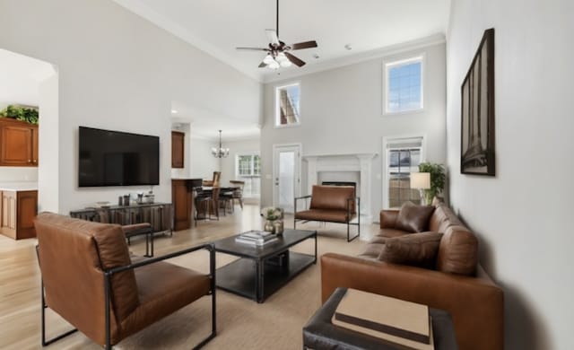 living room featuring light wood-type flooring, a towering ceiling, ceiling fan with notable chandelier, and crown molding