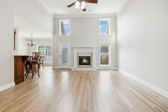 unfurnished living room featuring a towering ceiling, ornamental molding, ceiling fan with notable chandelier, and light wood-type flooring