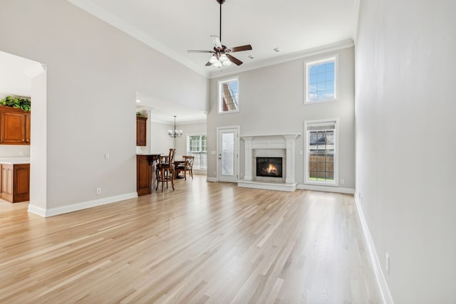 unfurnished living room with a high ceiling, ceiling fan with notable chandelier, light hardwood / wood-style flooring, and crown molding