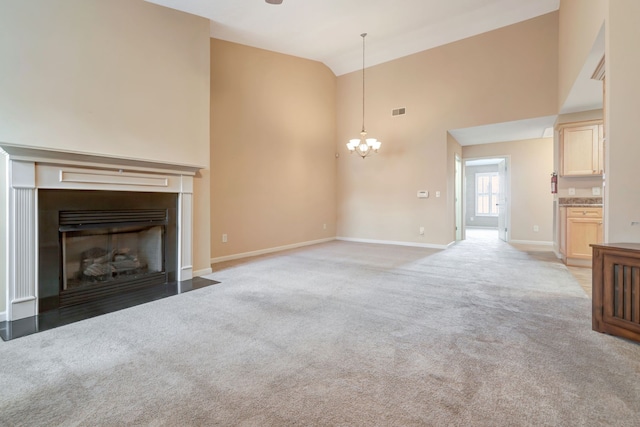 unfurnished living room featuring high vaulted ceiling, light colored carpet, and a notable chandelier