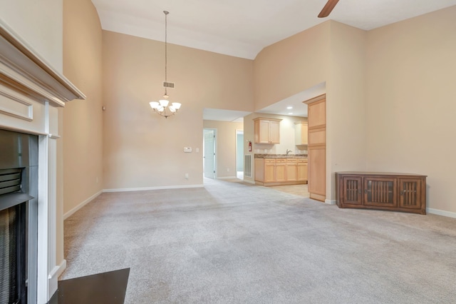 unfurnished living room with ceiling fan with notable chandelier, light carpet, and a high ceiling