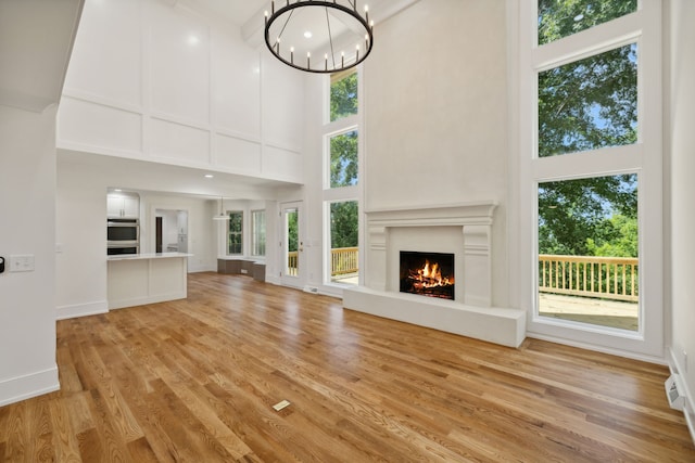 unfurnished living room with a notable chandelier, light wood-type flooring, and a high ceiling