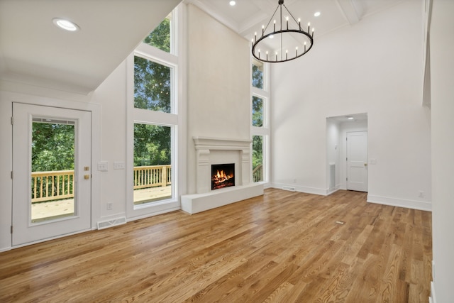 unfurnished living room featuring a chandelier, a high ceiling, light hardwood / wood-style floors, and beamed ceiling