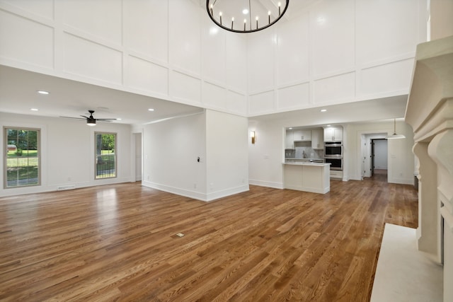 unfurnished living room featuring a high ceiling, ceiling fan with notable chandelier, and hardwood / wood-style flooring