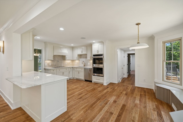 kitchen with white cabinetry, stainless steel appliances, premium range hood, kitchen peninsula, and light wood-type flooring