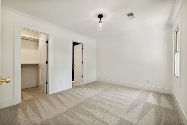 unfurnished bedroom with light carpet, a walk in closet, a closet, and crown molding