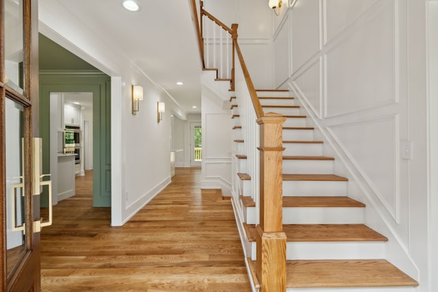 stairs with wood-type flooring and crown molding