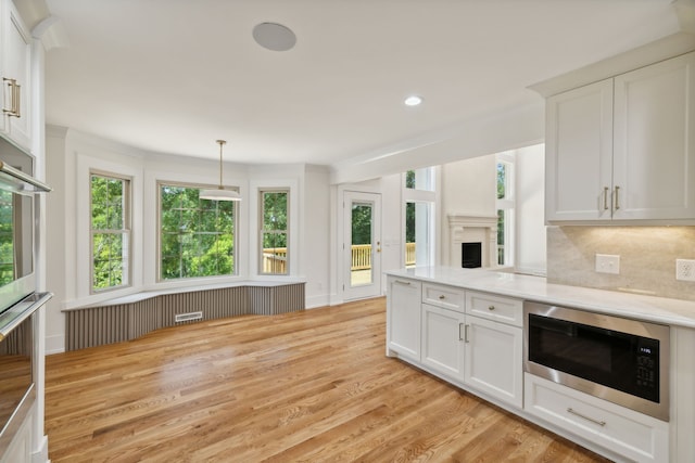 kitchen featuring white cabinetry, light wood-type flooring, decorative light fixtures, and appliances with stainless steel finishes