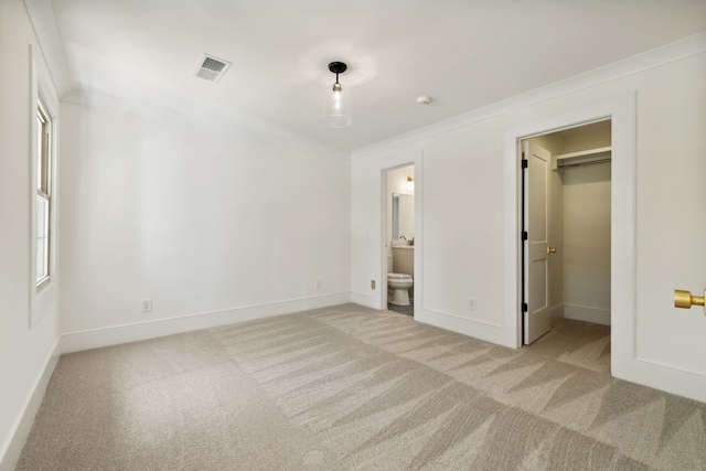 unfurnished bedroom featuring ensuite bath, a spacious closet, light colored carpet, a closet, and ornamental molding