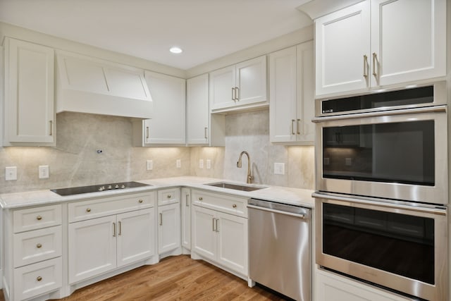 kitchen featuring sink, stainless steel appliances, tasteful backsplash, light hardwood / wood-style floors, and white cabinets