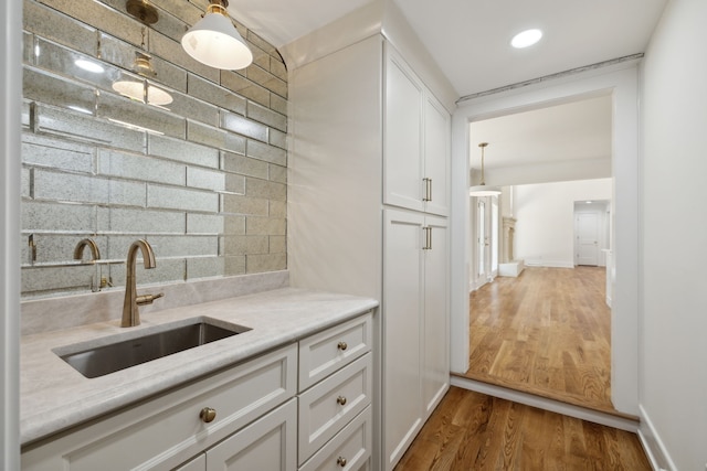 kitchen featuring light stone countertops, sink, tasteful backsplash, hardwood / wood-style floors, and white cabinets