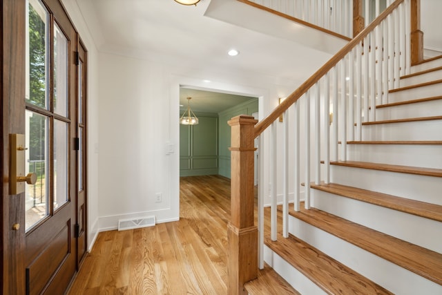 foyer entrance with a healthy amount of sunlight, light hardwood / wood-style floors, ornamental molding, and an inviting chandelier