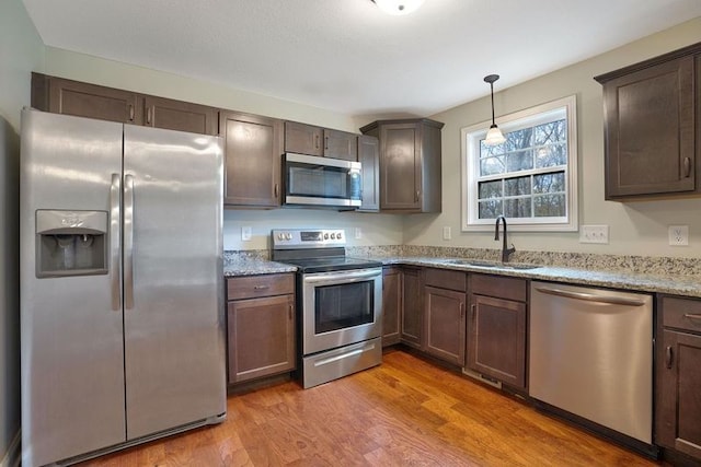 kitchen with appliances with stainless steel finishes, hardwood / wood-style flooring, light stone counters, and sink