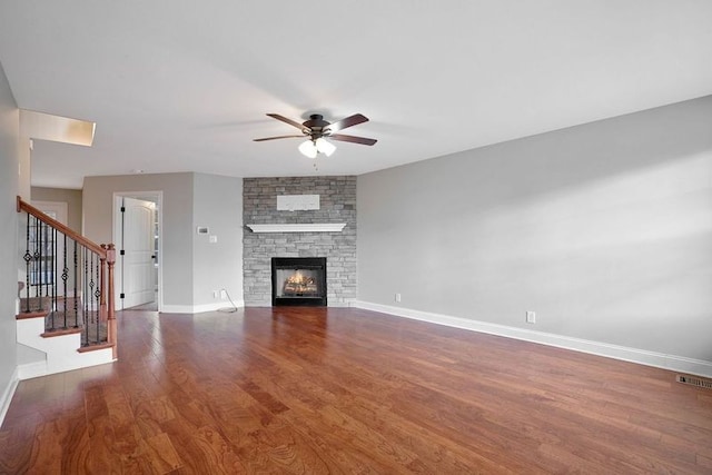 unfurnished living room with ceiling fan, a stone fireplace, and dark hardwood / wood-style flooring