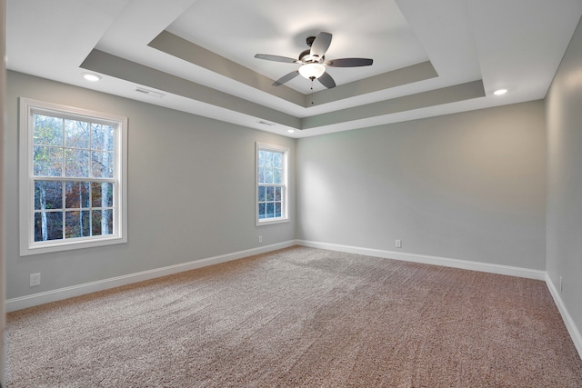 empty room with a tray ceiling, ceiling fan, and a healthy amount of sunlight