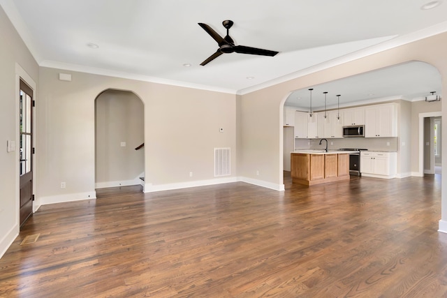 unfurnished living room featuring arched walkways, ceiling fan, a sink, visible vents, and dark wood-style floors