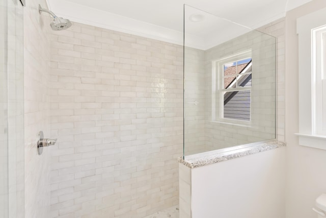 bathroom with ornamental molding and tiled shower