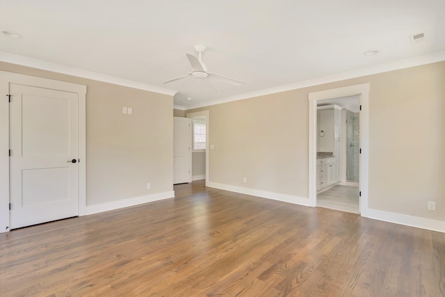 empty room with ornamental molding, wood finished floors, a ceiling fan, and baseboards