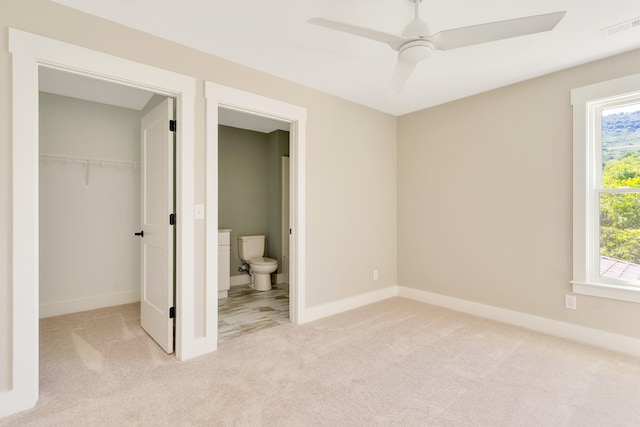 unfurnished bedroom featuring ceiling fan, light colored carpet, ensuite bath, and a closet