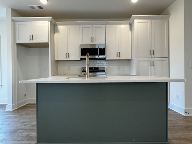 kitchen with tasteful backsplash, stainless steel appliances, white cabinets, and a center island with sink