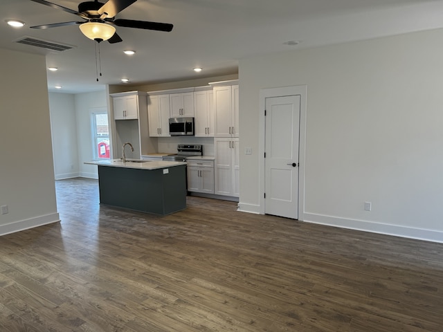 kitchen featuring appliances with stainless steel finishes, white cabinetry, sink, dark wood-type flooring, and a center island with sink