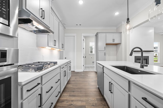 kitchen with a sink, light countertops, under cabinet range hood, appliances with stainless steel finishes, and crown molding