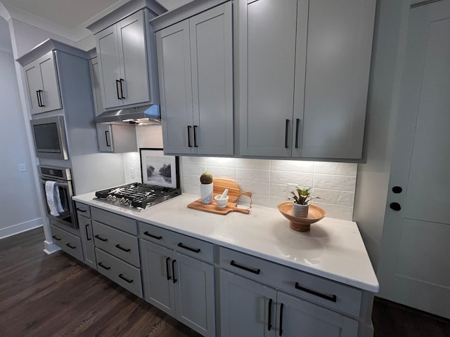 kitchen featuring under cabinet range hood, decorative backsplash, gray cabinets, dark wood-style floors, and stainless steel appliances