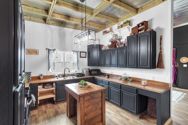 kitchen with pendant lighting, wood counters, black appliances, sink, and light wood-type flooring