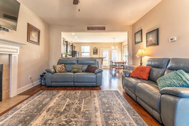 living room with ceiling fan with notable chandelier, dark wood-type flooring, and a tiled fireplace