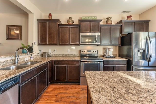 kitchen with light stone countertops, dark hardwood / wood-style flooring, dark brown cabinetry, stainless steel appliances, and sink