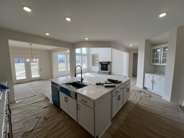 kitchen featuring white cabinets, dishwashing machine, open floor plan, and a stone fireplace