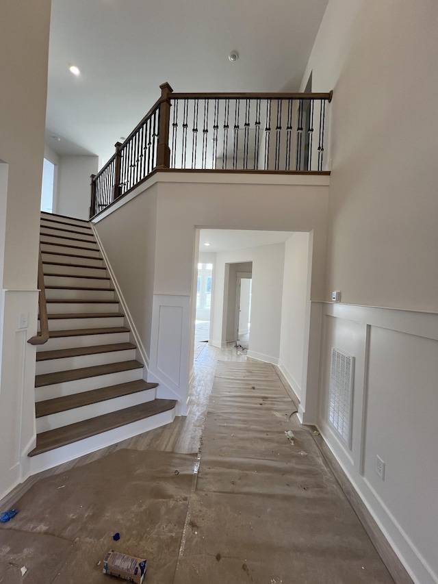 staircase featuring visible vents, a decorative wall, a high ceiling, wainscoting, and wood finished floors