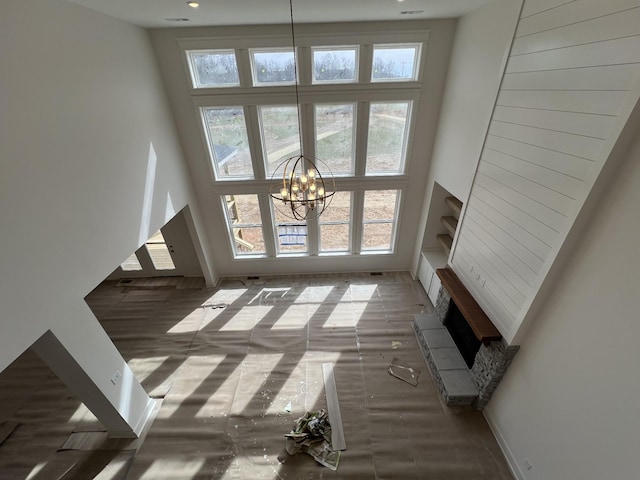 unfurnished living room featuring a high ceiling, baseboards, a fireplace with raised hearth, and a notable chandelier