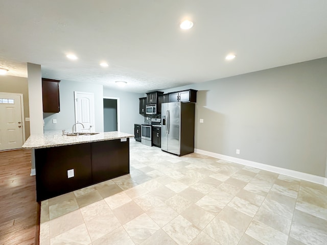 kitchen with kitchen peninsula, appliances with stainless steel finishes, light wood-type flooring, light stone countertops, and sink