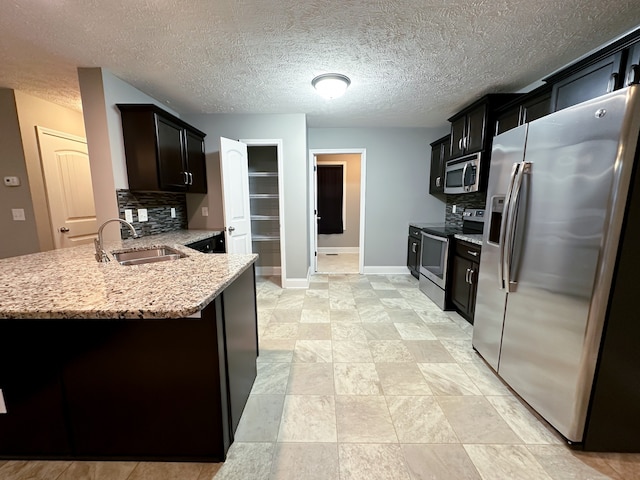 kitchen featuring sink, decorative backsplash, a textured ceiling, appliances with stainless steel finishes, and kitchen peninsula