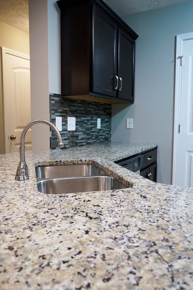 kitchen with decorative backsplash, light stone counters, sink, and a textured ceiling