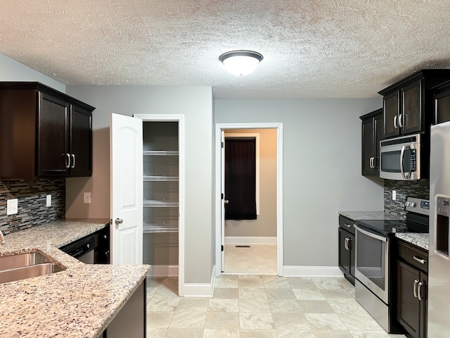 kitchen featuring sink, a textured ceiling, appliances with stainless steel finishes, tasteful backsplash, and light stone counters