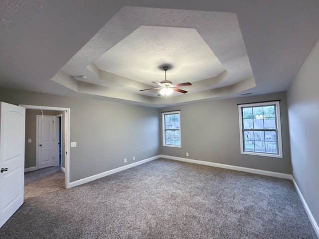 carpeted empty room with a textured ceiling, a tray ceiling, plenty of natural light, and ceiling fan