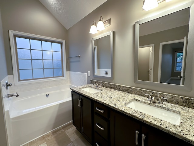 bathroom with a textured ceiling, a bathing tub, vanity, and vaulted ceiling