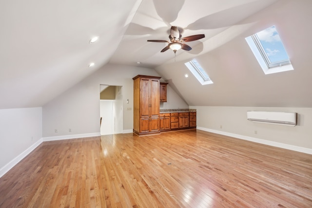 additional living space with a wall unit AC, lofted ceiling with skylight, light hardwood / wood-style flooring, and ceiling fan