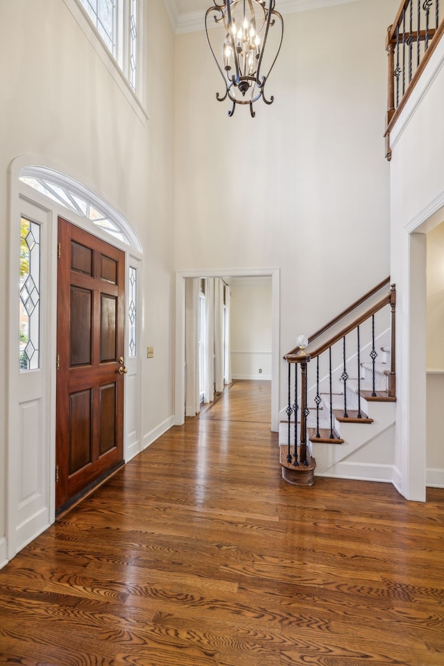 foyer entrance with a notable chandelier, crown molding, a towering ceiling, and dark wood-type flooring