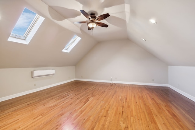 additional living space with a wall mounted air conditioner, ceiling fan, lofted ceiling with skylight, and light hardwood / wood-style flooring