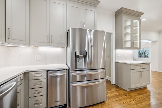 kitchen with gray cabinetry, crown molding, appliances with stainless steel finishes, and light hardwood / wood-style flooring