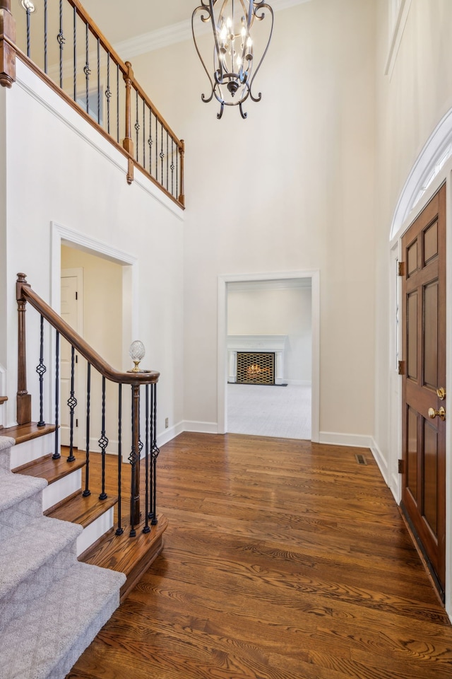 entrance foyer with a notable chandelier, dark hardwood / wood-style flooring, a towering ceiling, and ornamental molding