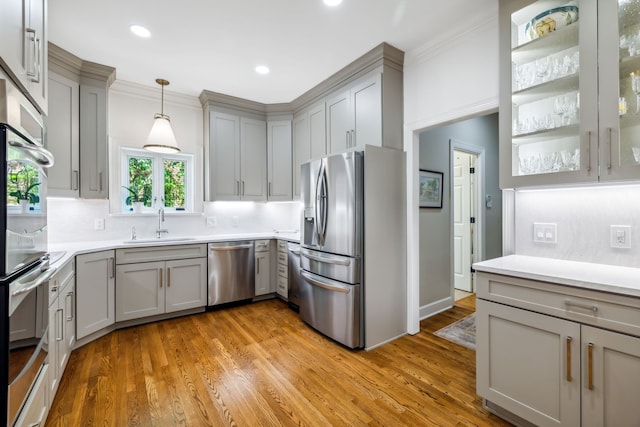 kitchen with appliances with stainless steel finishes, ornamental molding, sink, light hardwood / wood-style floors, and hanging light fixtures