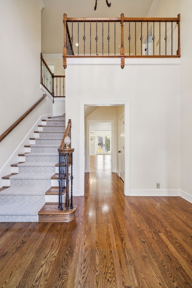 entryway featuring wood-type flooring, ornamental molding, and a towering ceiling