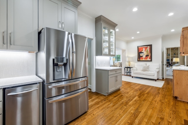 kitchen with ornamental molding, stainless steel appliances, light hardwood / wood-style flooring, and gray cabinetry