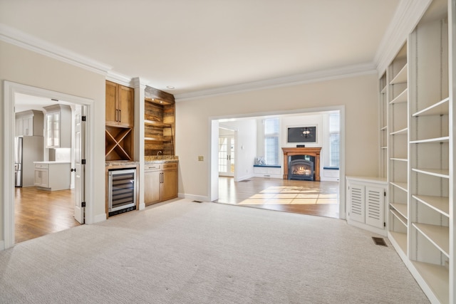 unfurnished living room featuring sink, crown molding, wine cooler, and light carpet