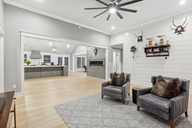 living room with wood walls, lofted ceiling, crown molding, ceiling fan, and light hardwood / wood-style floors