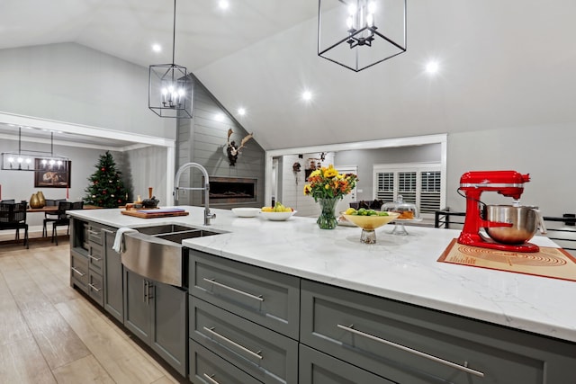 kitchen with gray cabinets, light stone counters, sink, and vaulted ceiling